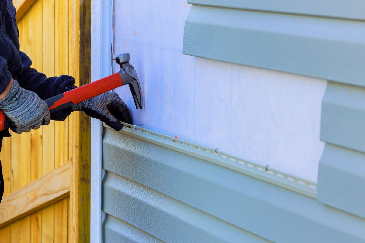 worker repairing blue grass siding